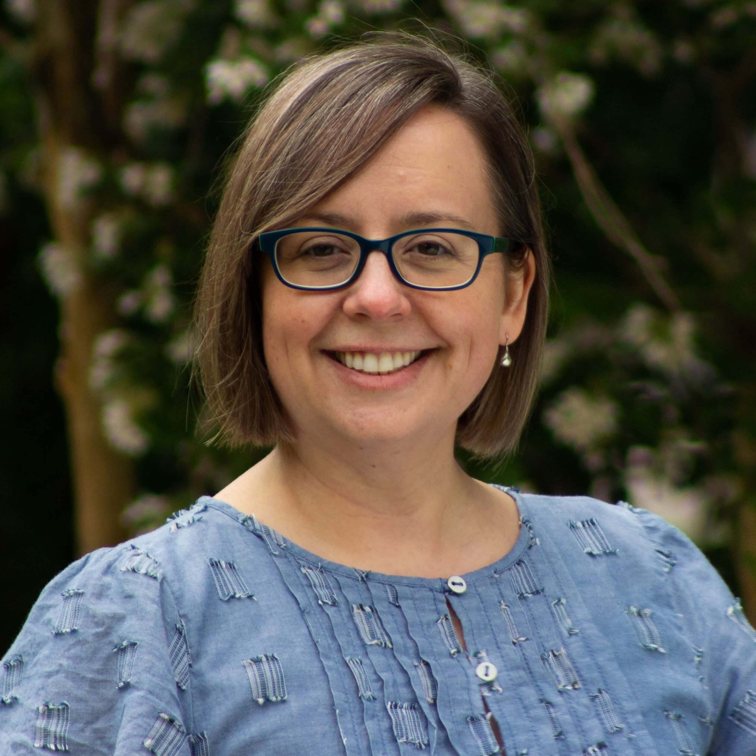 A headshot of Dr. Sarah Estelle standing before a flowering tree smiling.